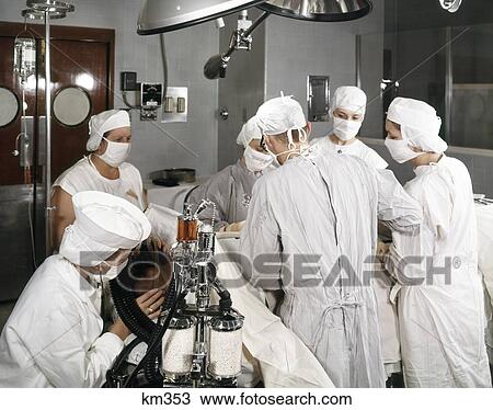Stock Image - 1960S Operating Room Team With Scrub And Circulating Nurse Two Surgeons Anesthetist Supervisor And Patient. Fotosearch