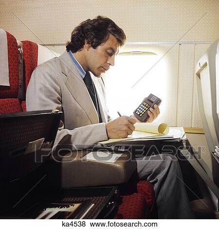 Stock Photo - 1970S 1980S Business Man Aboard Plane Working On Papers Holding Calculator In Hand . Fotosearch