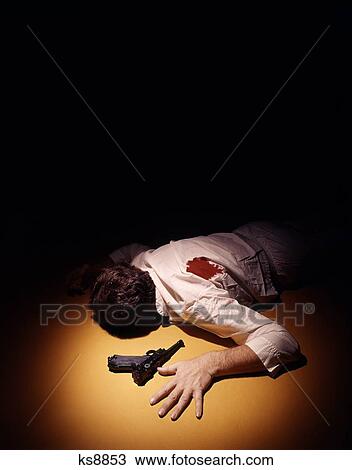 Stock Image - 1970S Anonymous Man Bloody Shirt Gun Shot Wound In Back Lying Face Down In Spotlight Beside Automatic Pistol. Fotosearch