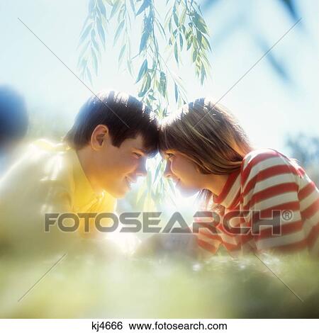 Stock Photograph - 1970S Teenage Boy And Girl Couple Lying In The Grass Head To Head Romantic Soft Focus Pose . Fotosearch