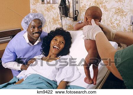 Stock Image - 1980S African American Mom And Dad View Newborn Infant In Hospital Berthing Room . Fotosearch