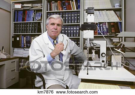 Stock Photograph - 1980S Doctor Sitting At Microscope Holding Glasses Looking At Camera . Fotosearch