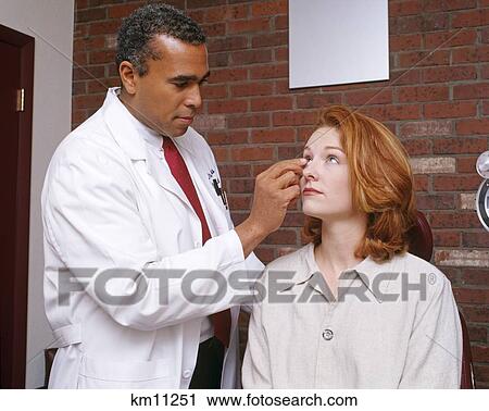 Stock Image - 1990S African American Man Optometrist Putting Contact Lens In Caucasian Woman'S Eye . Fotosearch