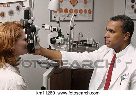 Stock Image - 1990S African American Optometrist Examining Red Haired Woman'S Eyes . Fotosearch