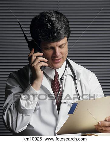 1990S Doctor Working At His Desk Talking On Cordless Telephone Reading Patient File View Large Photo Image Stock Photography - 1990S Doctor Working At His Desk Talking On Cordless Telephone Reading Patient File . Fotosearch