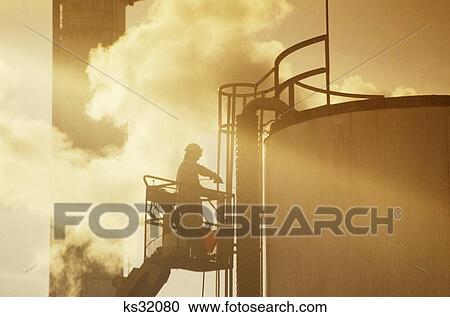 1990S Man Anonymous Refinery Worker On Lift Outside Storage Tank Silhouetted Against Smoke View Large Photo Image Stock Image - 1990S Man Anonymous Refinery Worker On Lift Outside Storage Tank Silhouetted Against Smoke . Fotosearch