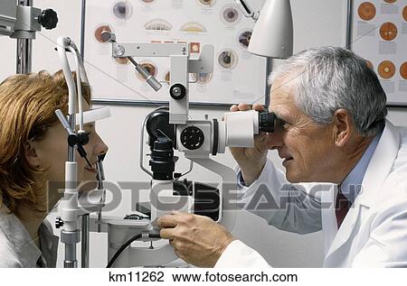 Stock Image - 1990S Older Male Optometrist Examining Red Haired Woman'S Eyes . Fotosearch