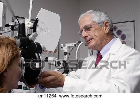 Picture - 1990S Senior Male Ophthalmologist Examining Red Haired Woman'S Eyes . Fotosearch