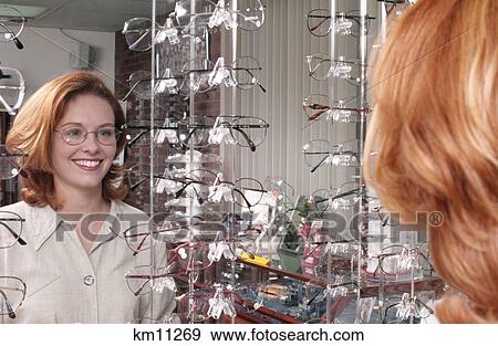 Stock Photo - 1990S Smiling Woman Trying On New Glasses Looking At Herself In A Mirror . Fotosearch