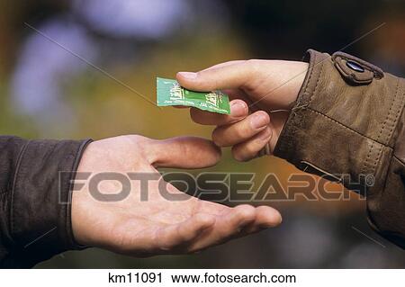 Stock Image - 1990S Young Woman Passing Condom To Young Man Hand To Hand . Fotosearch