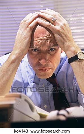 Stock Image - 2000S Stressed Businessman At Desk Holding Head In Hands . Fotosearch