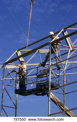 Stock Image - Construction Workers On Cherry Picker Crane Working On Metal Frame. Fotosearch