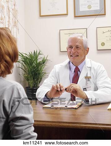 Stock Image - Male Physician Smiling At Anonymous Woman Patient In Office . Fotosearch