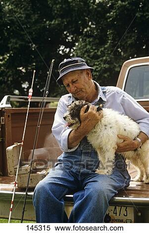 Stock Photography - Man On Back Of Pickup With Fishing Gear Holding Dog . Fotosearch