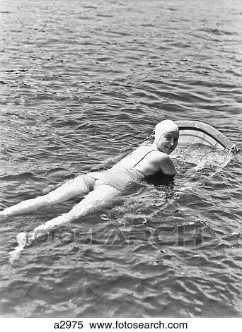 1930S 1940S Woman Wear Bathing Cap One Piece Suit Lying On Aqua Ski Board Look At Camera Over Shoulder Muskoka Lake Canada View Large Photo Image Stock Photography - 1930S 1940S Woman Wear Bathing Cap One Piece Suit Lying On Aqua Ski Board Look At Camera Over Shoulder Muskoka Lake Canada. Fotosearch