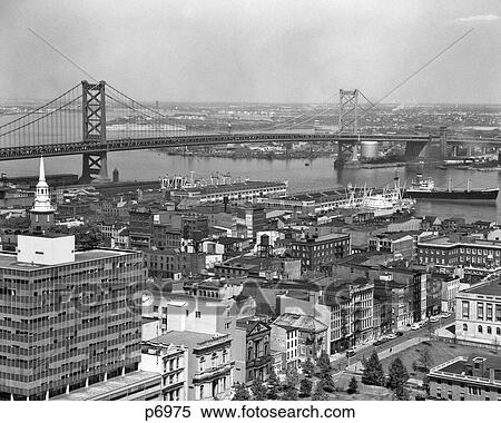 Stock Photography - 1950S Philadelphia Pa Usa Looking Northeast Past Delaware River Waterfront To Benjamin Franklin Suspension Bridge To Camden Nj. Fotosearch