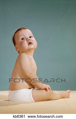 Stock Image - 1960S 1970S Baby Sitting Wearing Diaper Looking Up Over Shoulder Superior Facial Expression. Fotosearch