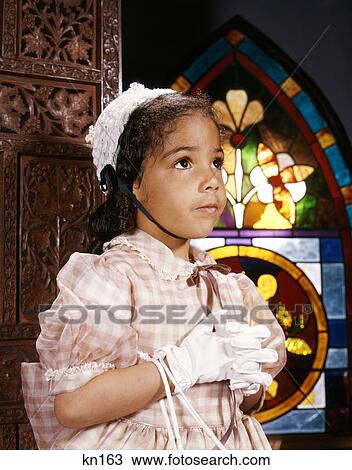 Stock Image - 1960S African American Girl In Church By Stained Glass Window Wearing Easter Dress Hat And White Gloves . Fotosearch