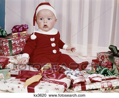 Stock Image - 1960S Amazed Baby In Santa Suit Sitting Among Wrapped Presents . Fotosearch