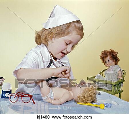 Stock Image - 1960S Little Girl Dressed Up As A Nurse Taking Care Of Her Doll. Fotosearch