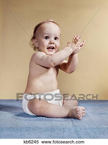 Stock Photography - 1960S Sitting Smiling Baby Clapping Hands Looking At Camera. Fotosearch