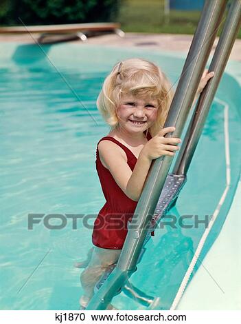 Stock Image - 1960S Smiling Blond Girl Climbing Swimming Pool Ladder Wearing Red Bathing Suit Looking At Camera. Fotosearch