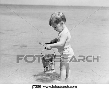 1930S 1940S Boy Toddler On Beach With Shovel And Sand Pail Bucket Summer Fun Seashore Play View Large Photo Image Stock Photograph - 1930S 1940S Boy Toddler On Beach With Shovel And Sand Pail Bucket Summer Fun Seashore Play. Fotosearch