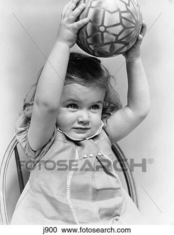 1930S 1940S Little Girl Toddler Holding Toy Ball Above Her Head With Both Arms View Large Photo Image Stock Image - 1930S 1940S Little Girl Toddler Holding Toy Ball Above Her Head With Both Arms. Fotosearch