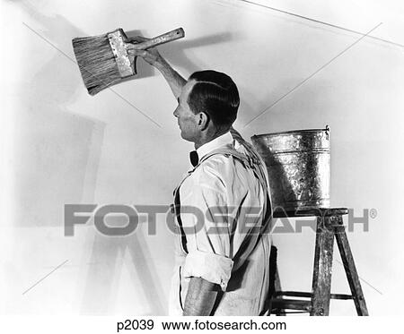 Stock Photo - 1930S 1940S Man In White Overalls By Step Ladder Zinc Pail Bucket Applying Paint Glue With Large Brush To Prepare For Wallpaper. Fotosearch
