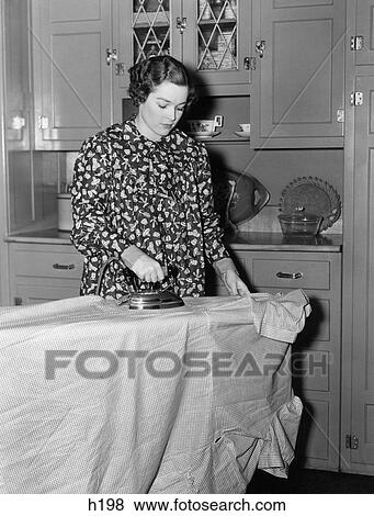 1930S 1940S Woman Wearing Printed Smock Apron Standing Ironing Board Pushing Electric Iron View Large Photo Image Stock Photo - 1930S 1940S Woman Wearing Printed Smock Apron Standing Ironing Board Pushing Electric Iron. Fotosearch