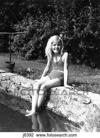 1930S 1940S Young Girl Sitting On Stone Wall Of Lake Pond Feet In Water Wearing Bathing Suit With Belt Blonde View Large Photo Image Stock Image - 1930S 1940S Young Girl Sitting On Stone Wall Of Lake Pond Feet In Water Wearing Bathing Suit With Belt Blonde. Fotosearch