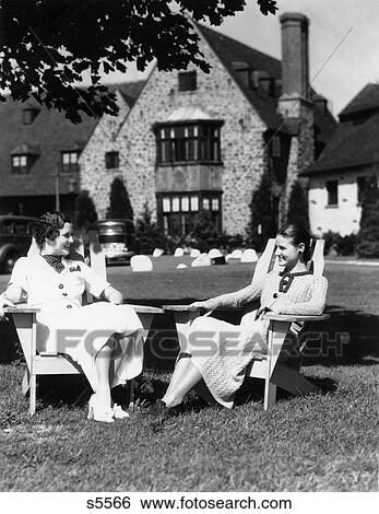 1930S Two Women Sitting In Adirondack Lawn Chairs In Front Of Stone Estate House Talking View Large Photo Image Stock Photograph - 1930S Two Women Sitting In Adirondack Lawn Chairs In Front Of Stone Estate House Talking . Fotosearch