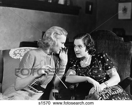 Stock Image - 1930S Two Women Sitting In Chairs In Private Conversation Woman Has Hand To Side Of Mouth To Tell Secret. Fotosearch