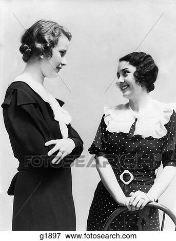 Stock Photo - 1930S Two Women Smiling Talking One Standing Arms Folded Other Wearing Polka Dot Dress With White Collar. Fotosearch