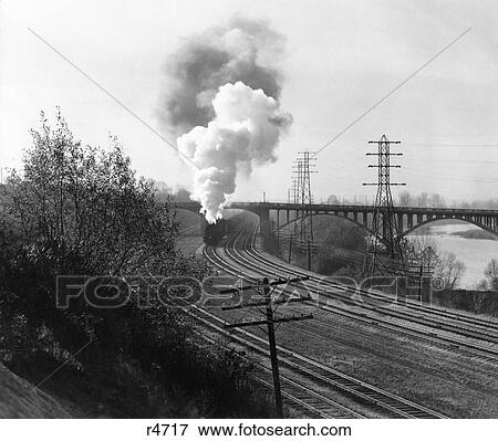 Stock Photo - 1940S Aerial Of Train Traveling Along River Under Bridge Billowing Smoke Near Columbus Ohio. Fotosearch
