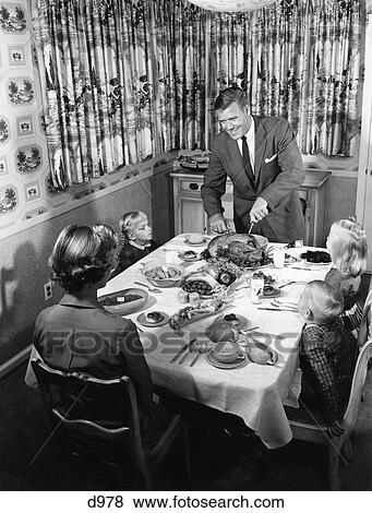 Stock Photo - 1950S Family Of 5 Thanksgiving Holiday Meal Mom Dad Man Woman 3 Kids Boys Girls At Dining Room Table Father Carving Turkey. Fotosearch