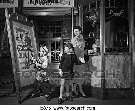 Stock Photography - 1950S Mother Taking Kids To Movies Buying Tickets To A Western Boy Wearing Cowboy Costume. Fotosearch
