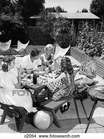 Picture - 1960S Family Sitting At Picnic Table In Backyard Eating Hamburgers. Fotosearch
