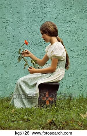1960S Pensive Young Teenage Girl Holding Long Stem Flower Sitting Bench Outdoors Profile Wearing Granny Dress View Large Photo Image Stock Photograph - 1960S Pensive Young Teenage Girl Holding Long Stem Flower Sitting Bench Outdoors Profile Wearing Granny Dress . Fotosearch