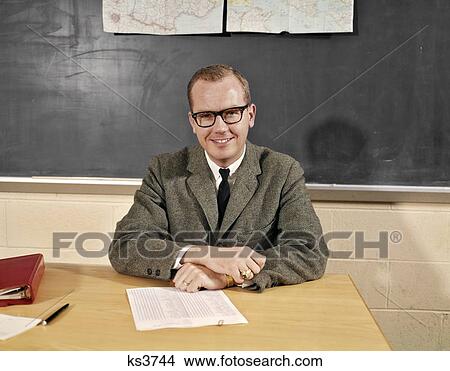 1960S Smiling Male School Teacher Sitting At Desk Wearing Eyeglasses Looking At Camera View Large Photo Image Picture - 1960S Smiling Male School Teacher Sitting At Desk Wearing Eyeglasses Looking At Camera. Fotosearch