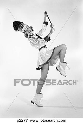 Stock Photo - 1960S Woman Majorette Band Uniform Short Skirt Boots Tassels Marching One Leg Up Holding Baton Smiling. Fotosearch