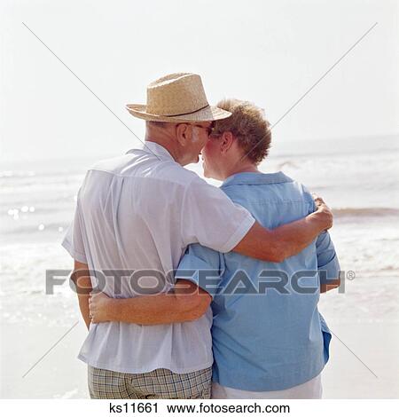 1970S Back View Retired Couple On Beach Man Whispering To Woman View Large Photo Image Stock Image - 1970S Back View Retired Couple On Beach Man Whispering To Woman . Fotosearch