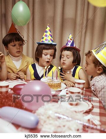 Stock Photography - 1970S Twin Girls And Other Children At Birthday Party Blowing Out Candles On Cake. Fotosearch