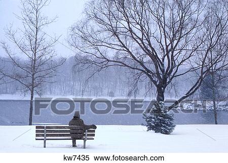 Stock Photography - Single Anonymous Silhouetted Man Sitting Alone On Cold Wintery Park Bench In Snow Looking At River. Fotosearch