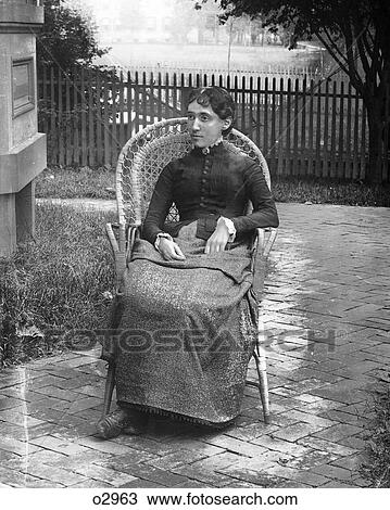Stock Image - 1890S 1900S Turn Of The 20Th Century Portrait Severe Woman Sitting In Wicker Chair In Backyard By House . Fotosearch