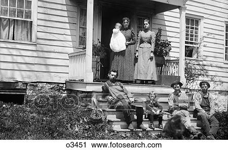 Stock Image - 1890S Group Portrait Family Adults Children Posing Sitting Standing On Front Porch Of House Looking At Camera. Fotosearch