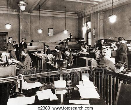 Stock Image - 1910s 1920s BUSINESS OFFICE WITH WOMEN SITTING AT DESKS IN BULLPEN AREA. Fotosearch