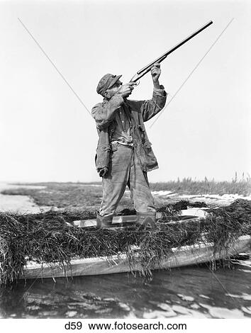 1920S Man Duck Hunting Standing In Sneakbox Boat In Marsh Aiming Shotgun Barnegat Bay New Jersey Usa View Large Photo Image Stock Photo - 1920S Man Duck Hunting Standing In Sneakbox Boat In Marsh Aiming Shotgun Barnegat Bay New Jersey Usa. Fotosearch