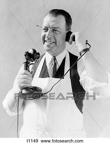 1920s MAN IN APRON BUTCHER COOK TALKING ON CANDLESTICK TELEPHONE PENCIL IN EAR View Large Photo Image Stock Photo - 1920s MAN IN APRON BUTCHER COOK TALKING ON CANDLESTICK TELEPHONE PENCIL IN EAR. Fotosearch