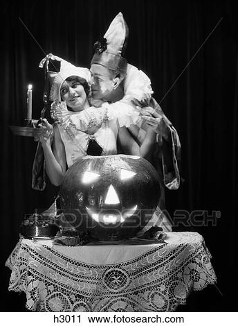 Stock Image - 1920S Romantic Couple Wearing Costumes With Large Carved Pumpkin Jack-O-Lantern On Table . Fotosearch